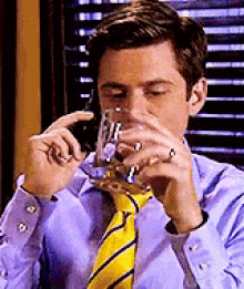 a man in a purple shirt and yellow tie is drinking a glass of water