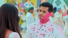 a man with pink paint on his face is looking at a woman in a crowd .