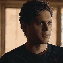 a close up of a man 's face with curly hair wearing a black sweater .