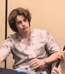 a young man is sitting at a table holding a microphone and making a funny face .