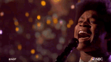 a man singing into a microphone with the nbc logo on the bottom right