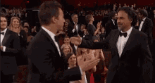 two men in tuxedos are kissing in front of a crowd of people .