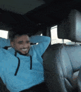 a man in a blue hoodie is sitting in the back seat of a car with his hands behind his head .