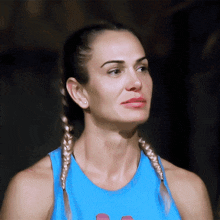a woman with braids wearing a blue tank top looks to the side