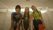 three girls are standing in a bathroom with one wearing a green top that says cotton