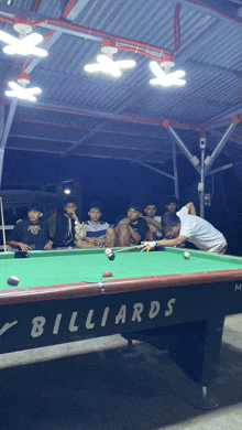 a group of young men are playing pool on a table that says billiards