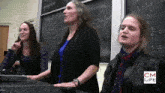 three women are standing in front of a blackboard with cm life written on it