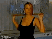 a woman in a black tank top is lifting a barbell in front of a sign that says oprah
