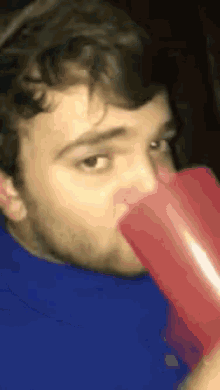 a man in a blue shirt is drinking from a red plastic cup