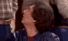 a man in a leather jacket is sitting in a chair and looking up at something .