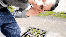 a man smells something in a manhole cover on the ground