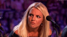 a blonde woman is making a funny face in front of a microphone .