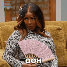 a woman sitting on a couch holding a fan with the word ooh written on it