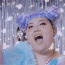 a woman with purple hair and a disco ball in the background is smiling