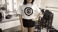 a woman is standing in a room wearing a white shirt with a black target on it .