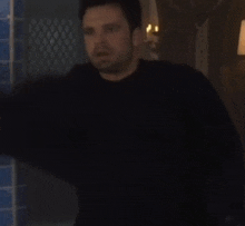 a man in a black sweater is standing in front of a window in a dark room .