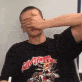 a man wearing a black shirt with the word slayer on it covering his eyes