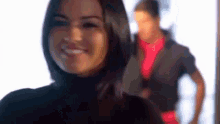 a woman is smiling and looking at the camera while a man is standing behind her .