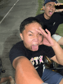 a man wearing a black shirt that says ' atr ' on it sticks his tongue out