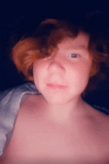 a shirtless person with red hair and blue eyes looks at the camera