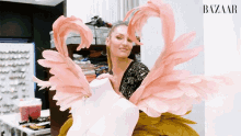 a woman is holding a mannequin with pink feathers and the word bazaar behind her