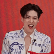 a young man wearing a blue and white floral shirt is smiling with his mouth wide open
