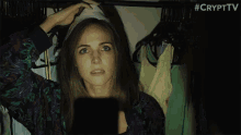 a woman is standing in a closet with clothes hanging on a rack and looking at something .