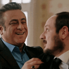 a man with a ring on his finger smiles while another man looks on