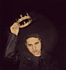 a man in a leather jacket is holding a gold crown above his head
