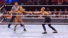 two women are wrestling in a wrestling ring with a referee in the background