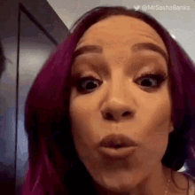 a woman with purple hair is blowing a kiss at the camera .