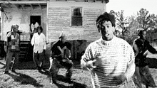 a black and white photo of a group of men dancing in front of a house .