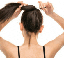 a woman is tying her hair into a bun with a rubber band .
