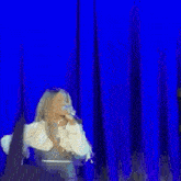 a woman is standing on a stage in front of a blue curtain holding a remote control .