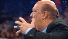 a bald man with a ring on his finger is sitting in front of a screen that says w live