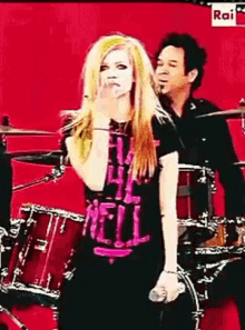a woman wearing a shirt that says " all hell " is singing into a microphone