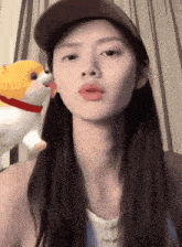 a woman with long hair wearing a baseball cap and a stuffed dog behind her