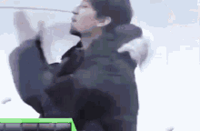 a man is standing in the snow with his arms outstretched and a green box in the background .