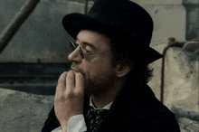 a man wearing a hat and glasses has his hand on his mouth