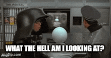 a man in a black helmet is talking to another man in a black helmet in front of a television .