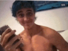 a shirtless man with blue hair is holding a camera with the number 8/8 in the corner