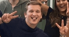 a man is sticking out his tongue while giving a peace sign .