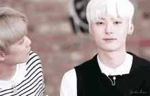 a man with white hair is standing next to another man in a striped shirt