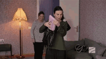 two women are standing in a living room with a lamp