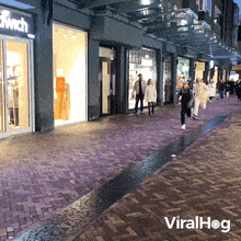 a group of people are walking down a brick sidewalk in front of a store called dwich