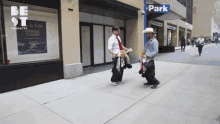 two men are walking down a sidewalk in front of a sign that says " park "