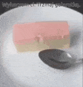 a white plate with a spoon and a piece of pink and white jelly on it