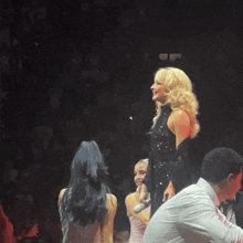 a blonde woman in a black dress is standing on a stage