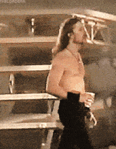 a man without a shirt is standing in front of a row of bleachers holding a cup