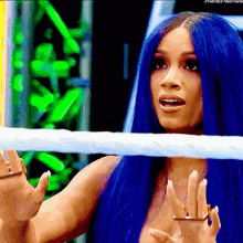a woman with blue hair is standing in a wrestling ring with her hands outstretched